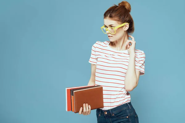 Женщина-студентка с книгами в руках на синем фоне и в желтых очках модель прически обрезанный вид — стоковое фото
