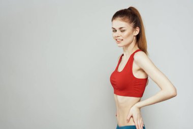 Kırmızı tişörtlü, arka planda bir kadın elleriyle spor jestleri yapıyor. Zayıf bir figür. 