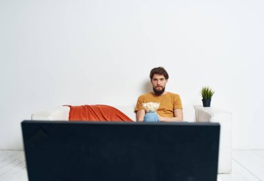 Kanepede patlamış mısırla televizyon izleyen genç adam ve kadın ve ekose yeşil çiçek.