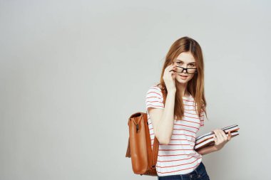 Sırtında not defteri ve sırt çantası olan bayan öğrenci bilim gözlüklerini kırpmış.