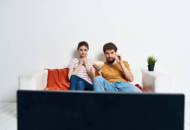 Bir adam ve bir kadın TV 'nin önündeki kanepede oturuyorlar ve yeşil bir çiçek evin içinde.