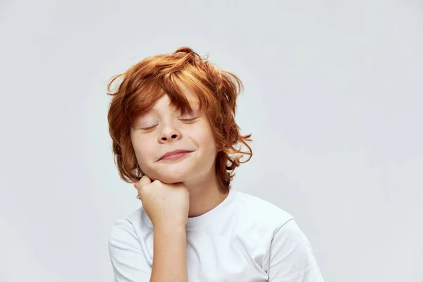 Rude włosy dziecko z zamkniętymi oczami trzyma rękę na podbródku przycięty widok uśmiech — Zdjęcie stockowe