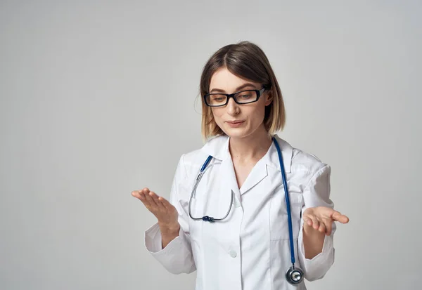 Enfermera mujer en un vestido médico gesto con las manos en un espacio de copia de fondo ligero —  Fotos de Stock