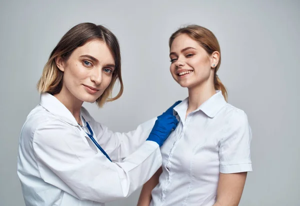 Szczęśliwa kobieta lekarz w niebieskich rękawiczkach i pacjentka w białym t-shirt stetoskop suknia medyczna — Zdjęcie stockowe