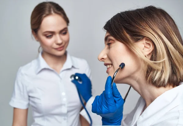 Composition doctor in a crowd and in blue gloves and a patient in a white T-shirt on a light background — Stock Photo, Image