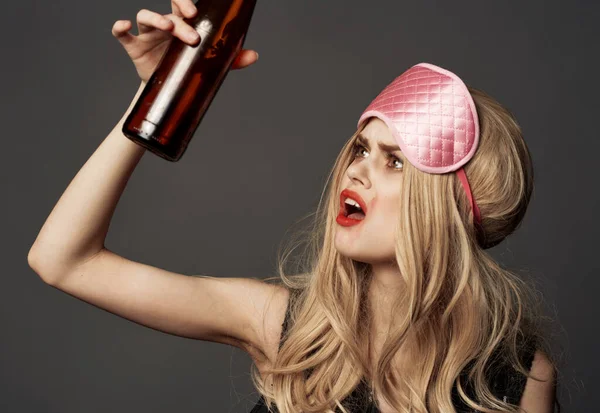 Mulher com uma garrafa de cerveja e uma máscara de dormir rosa — Fotografia de Stock