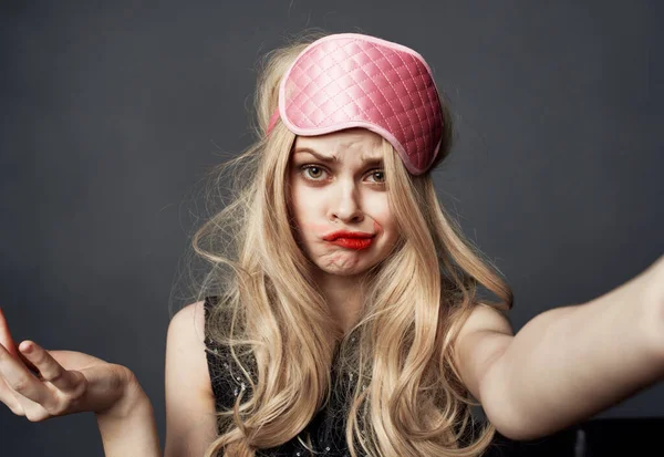 Eine betrunkene Blondine mit rosa Schlafmaske auf dem Kopf schmiert sich Lippenstift ins Gesicht — Stockfoto