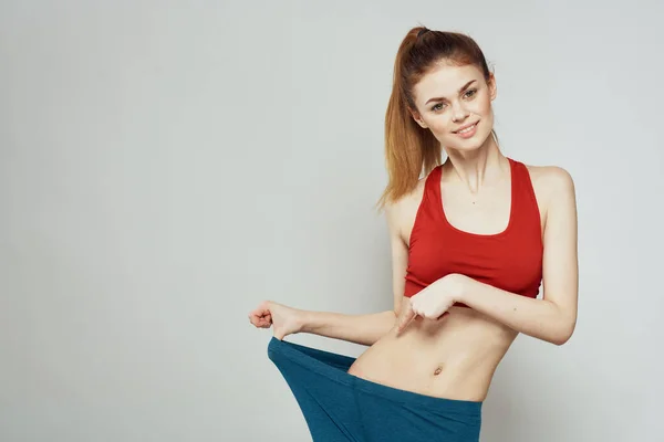 Una mujer con una camiseta roja sobre un fondo claro se dedica a gestos de fitness con las manos una figura delgada — Foto de Stock