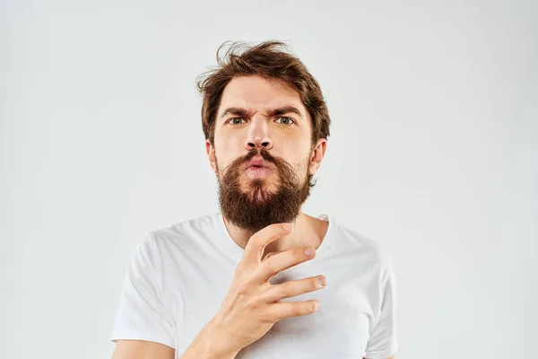 Емоційний бородатий чоловік у білій футболці жести зі світлим фоном своїми руками — стокове фото