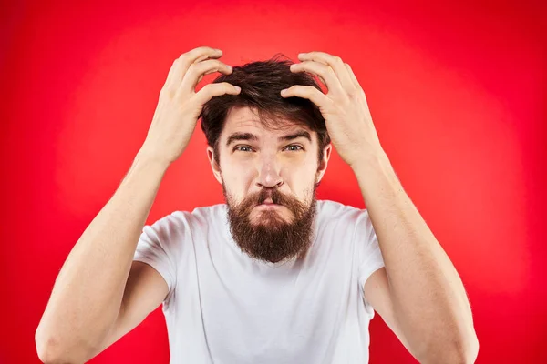 Емоційний жести бородатого чоловіка своїми руками в білій футболці агресія невдоволення червоним тлом — стокове фото