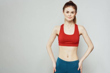 Kırmızı tişörtlü, arka planda bir kadın elleriyle spor jestleri yapıyor. Zayıf bir figür. 