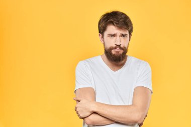 Sakallı adam duyguları, yüz ifadesi, beyaz tişört, sarı arka plan.