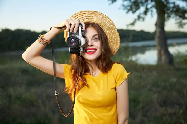 Woman holding camera looks into the camera lens red lips hat nature