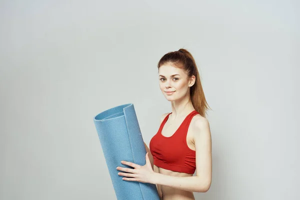 Vrouw houdt in de hand een mat voor fitness sport slanke figuur oefeningen lichte achtergrond — Stockfoto