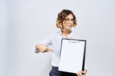 Elinde beyaz dökümanların olduğu bir klasör olan iş kadını arka planda ve saç stili gözlüklü model