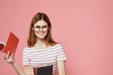 Elinde kitap tutan güzel bir kız öğrenci. El hareketleriyle el hareketi yapıyor. Pembe arka plan.
