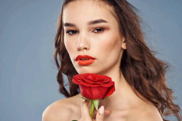 Portrait de femme avec rose rouge près du visage sur fond gris et maquillage cheveux bouclés — Photo