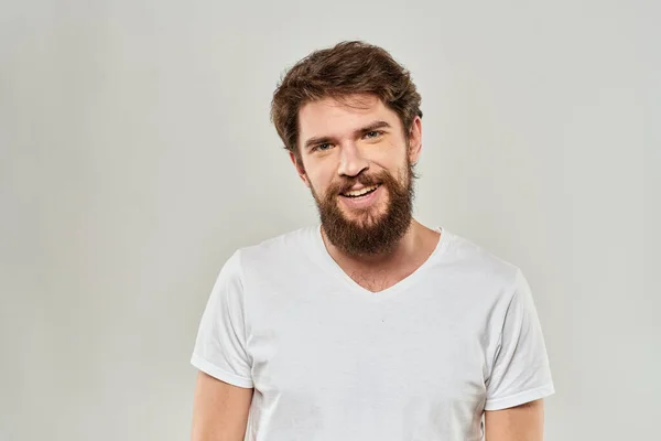 Man met baard gebaren met zijn handen in een witte t-shirt agressie licht achtergrond — Stockfoto