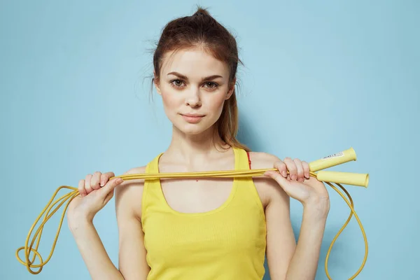 Atlayan halat tutan sportif bir kadın sarı atlet üst egzersiz jimnastik mavi arka plan — Stok fotoğraf