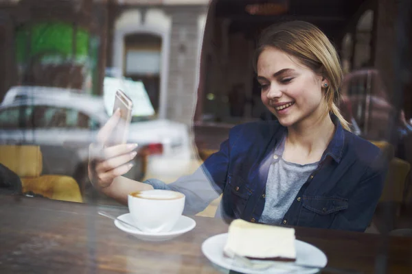Egy nő telefonnal a kezében egy kávézóban reggelizik. — Stock Fotó