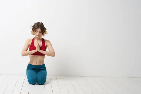 Una mujer en jeans azules practica yoga sobre un fondo claro en interiores y una figura delgada en gimnasia — Foto de Stock