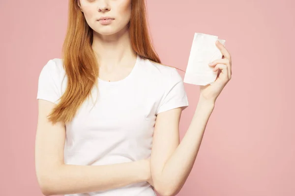 Piros hajú nő egy pad a kezében, és egy fehér póló egy rózsaszín háttér higiéniai ellátás a megjelenés — Stock Fotó
