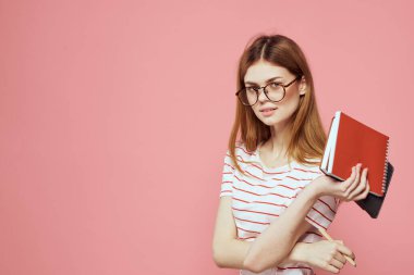 Elinde kitap tutan güzel bir kız öğrenci. El hareketleriyle el hareketi yapıyor. Pembe arka plan.