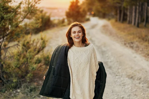 Mujer en una chaqueta caminando por la carretera cerca del bosque —  Fotos de Stock