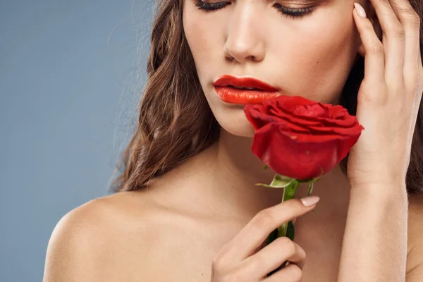 Vrouw portret met rode roos in de buurt van het gezicht op grijze achtergrond en make-up krullend haar — Stockfoto