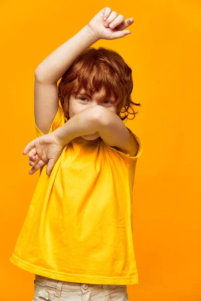 Vidám vörös fiú, sárga pólóban táncol. — Stock Fotó