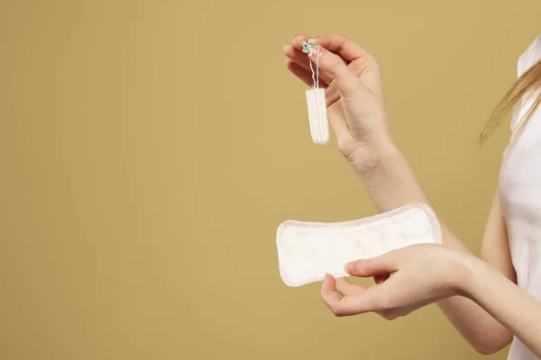 Menina com um tampão e uma almofada na mão em um fundo bege vista recortada de dias críticos menstruação — Fotografia de Stock