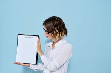 Mavi arka planda bir klasörde evrakları olan ve yüzünde açık renk gözlüklü bir iş kadını.