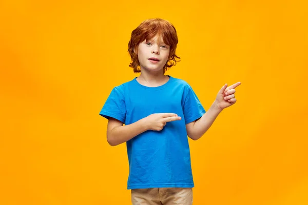 Rudowłosy chłopiec pokazujący kciuki na boku niebieski t-shirt styl życia Skopiuj przestrzeń — Zdjęcie stockowe