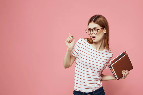 Studentka s poznámkovými bloky na růžovém pozadí gestikuluje s brýlemi na obličeji pruhované tričko model — Stock fotografie