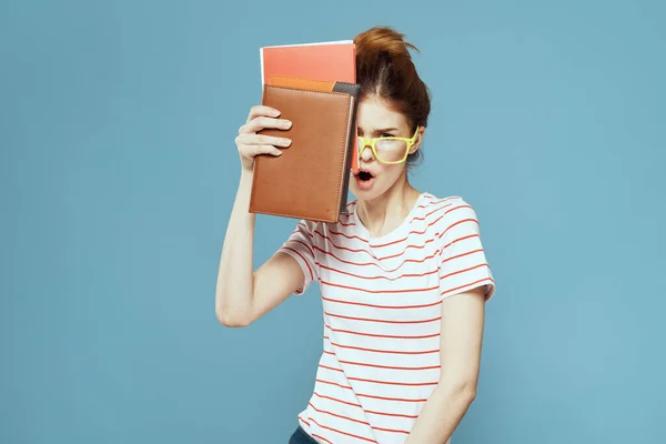 Vrouwelijke student met boeken in handen op een blauwe achtergrond en gele bril model kapsel bijgesneden uitzicht — Stockfoto