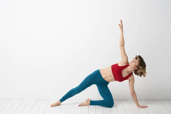 Una mujer en jeans azules practica yoga sobre un fondo claro en interiores y una figura delgada en gimnasia — Foto de Stock