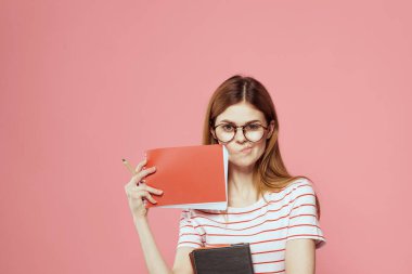 Elinde kitap tutan güzel bir kız öğrenci. El hareketleriyle el hareketi yapıyor. Pembe arka plan.