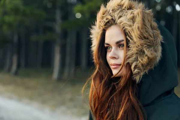 Mulher bonita em um casaco com um capuz olha para o lado em uma natureza de viagem — Fotografia de Stock