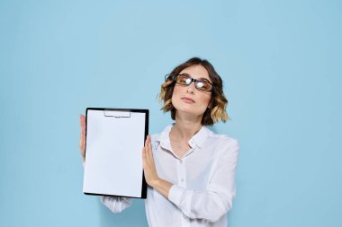 Mavi arka planda bir klasörde evrakları olan ve yüzünde açık renk gözlüklü bir iş kadını.