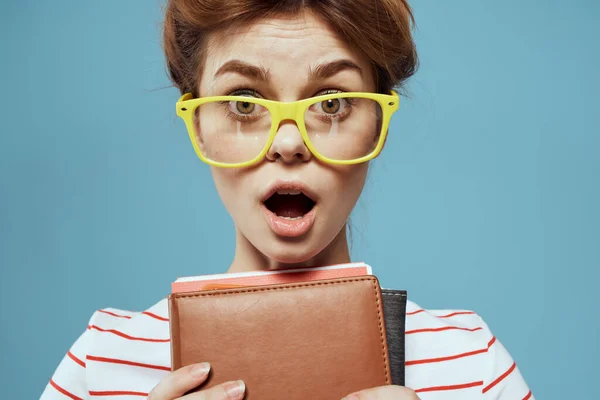 Красивая студентка с блокнотами и в желтых очках в синем учебном заведении — стоковое фото