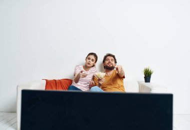 Bir adam ve bir kadın TV 'nin önündeki kanepede oturuyorlar ve yeşil bir çiçek evin içinde.