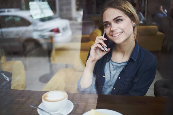 A nő egy kávézó telefonján kommunikál az asztalnál egy csésze kávéval a reggeli életvitelben. — Stock Fotó