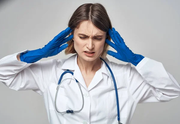 Emotional woman in blue medical gloves touches her head with her hands on a light background