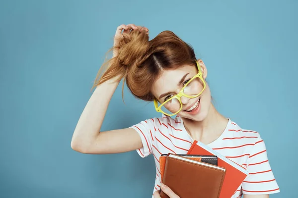 Estudante feminino enérgico com blocos de notas e óculos modelo fundo azul — Fotografia de Stock