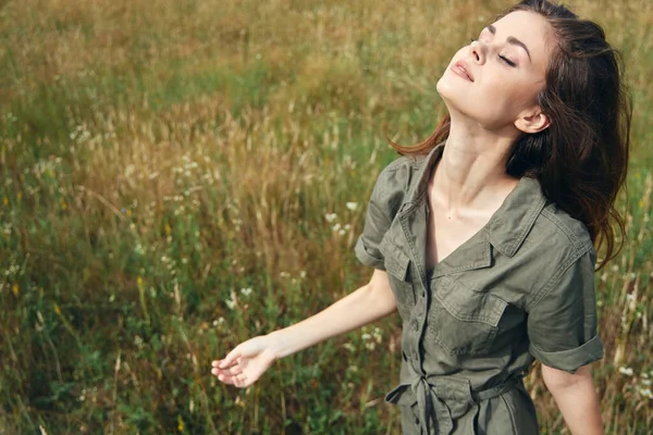 Woman in green jumpsuit looks up closed eyes enjoying nature