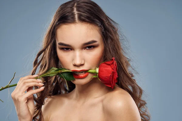 Portrait d'une femme avec une rose rouge dans les mains sur un fond gris épaules nues maquillage du soir — Photo