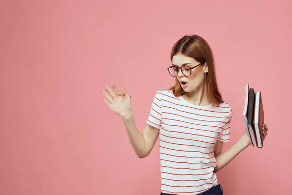 Studentka s poznámkovými bloky na růžovém pozadí gestikuluje s brýlemi na obličeji pruhované tričko model — Stock fotografie