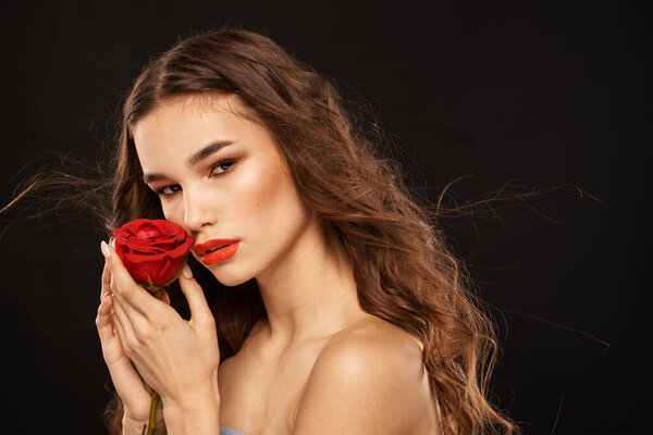 woman with a red rose on a dark background long hair makeup red lips