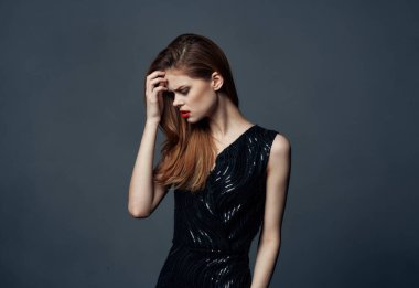 Gri arka planda, parlak makyajlı ve göz kapaklarında gölgeler olan siyah elbiseli duygusal kadın portresi.