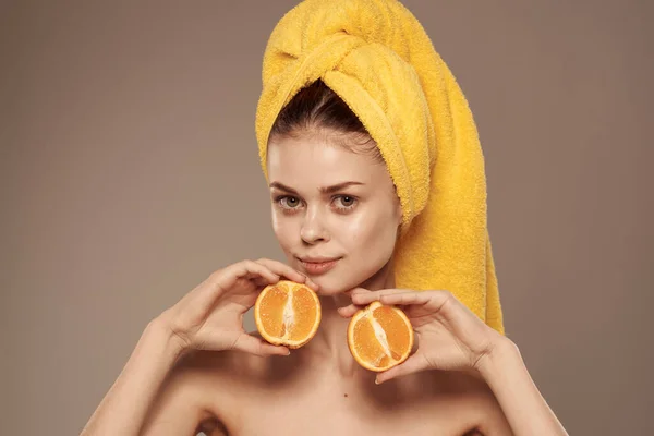 Pretty woman bared shoulders oranges in the hands of a yellow towel on her head — Stock Photo, Image